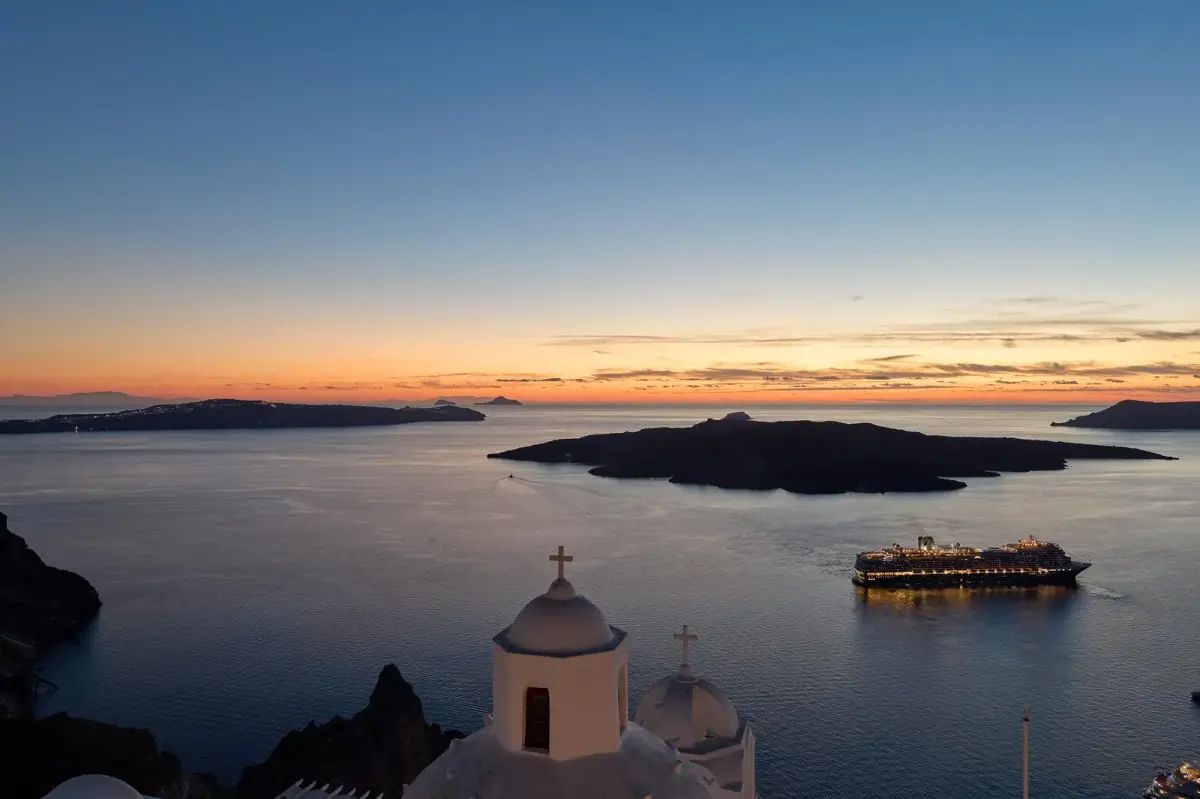 The caldera at dusk from Aroma Suites in Fira, with Nea Kameni, a lit cruise ship and church domes
