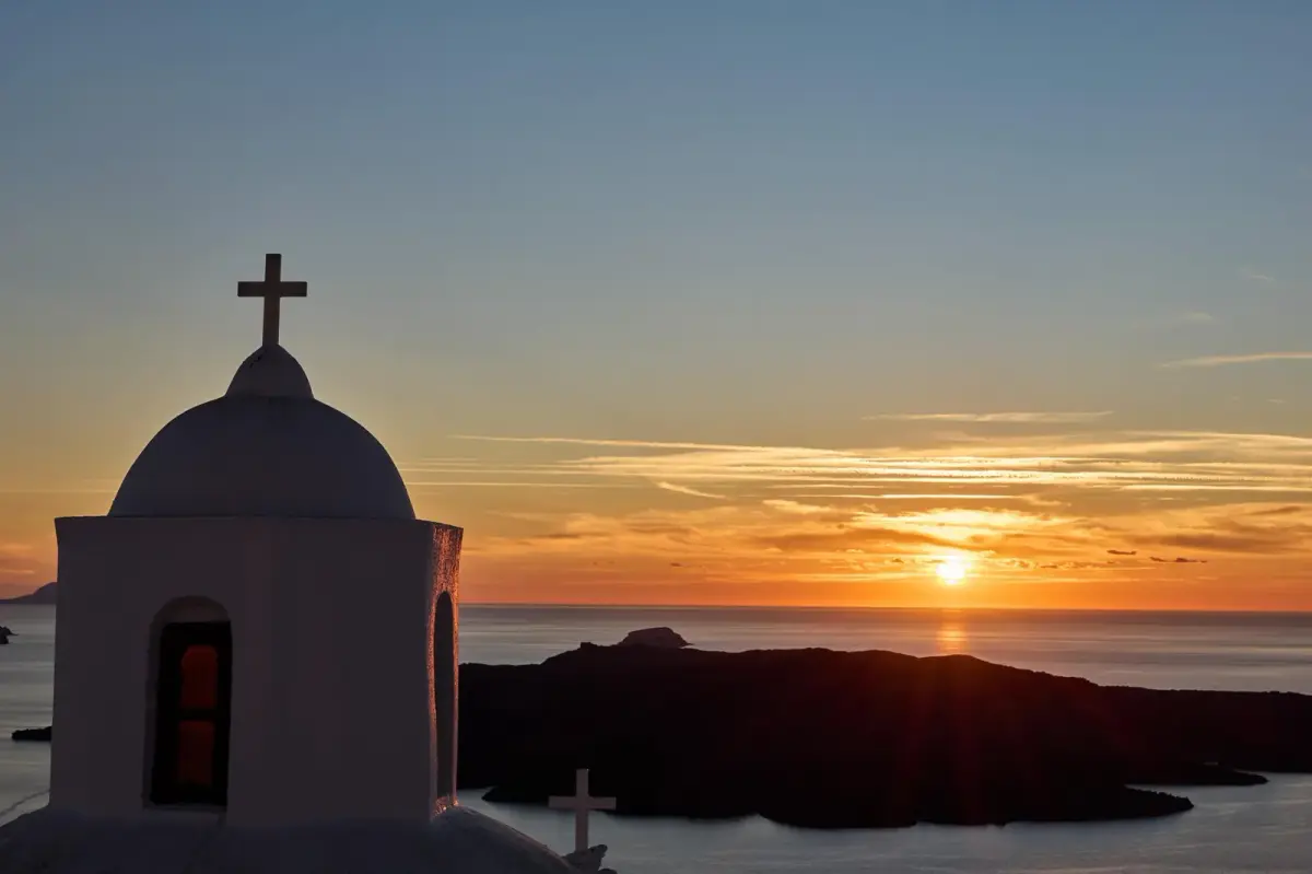 A church dome in silhouette against the sunset over the caldera, seen from Aroma Suites in Fira