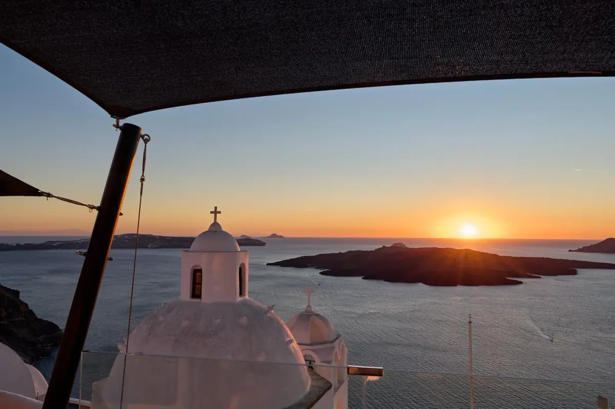 Sunset over the caldera and Nea Kameni from a shaded terrace at Aroma Suites, church domes below