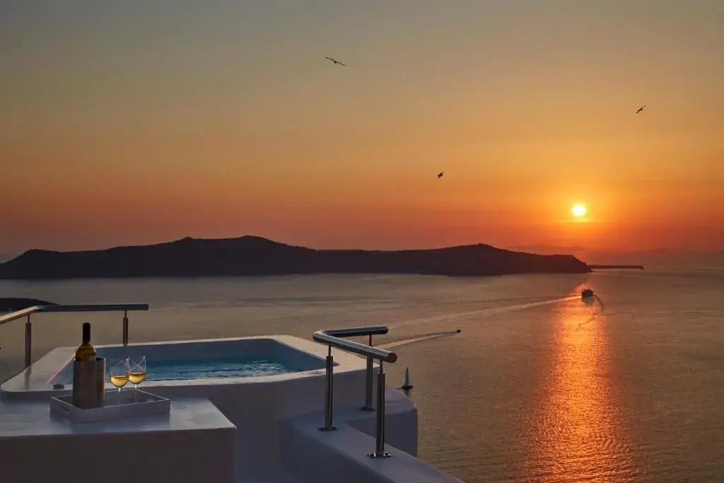 Outdoor jacuzzi on the private villa terrace at Aroma Suites, the sun setting over the caldera