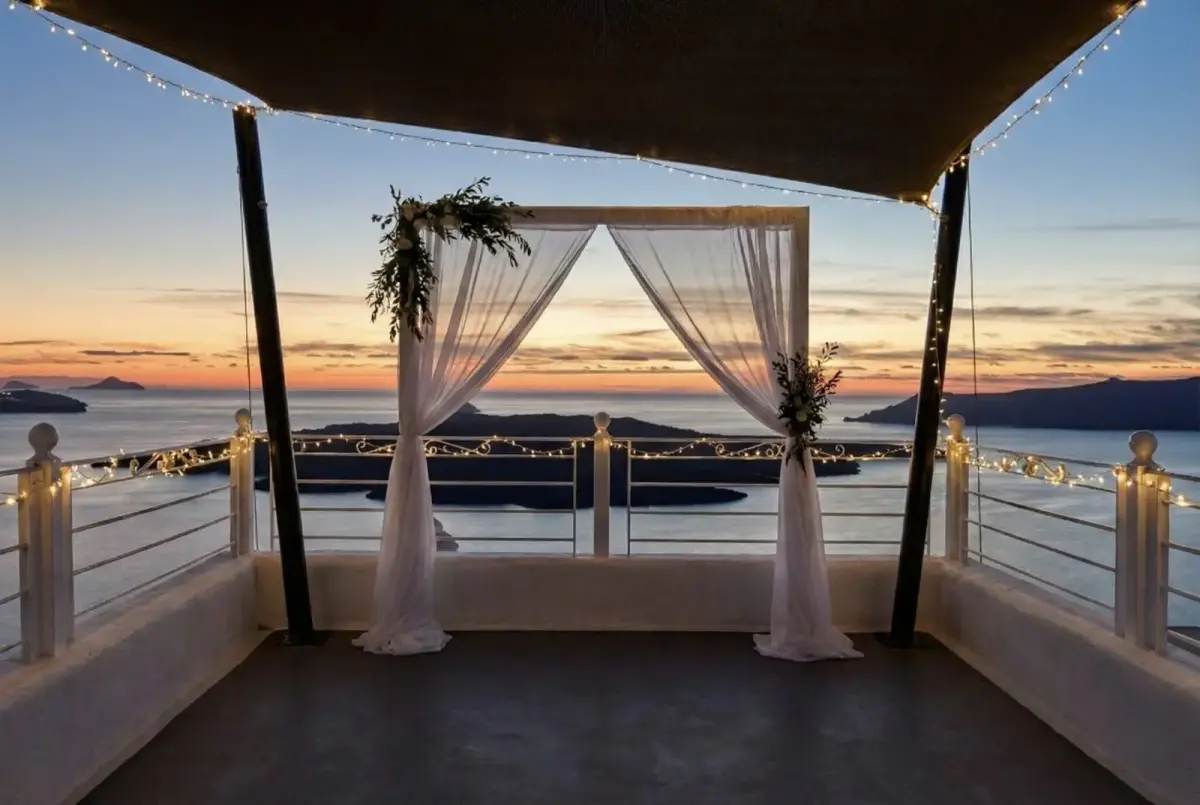 Wedding arch with white drapes and string lights on a terrace at Aroma Suites, the caldera at sunset behind