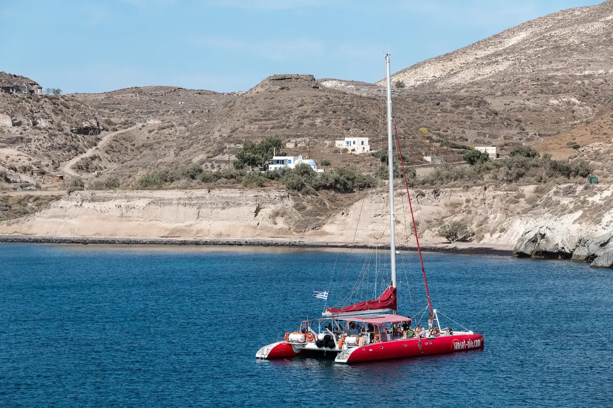 Red catamaran at anchor in a bay near Akrotiri, Santorini, people on deck