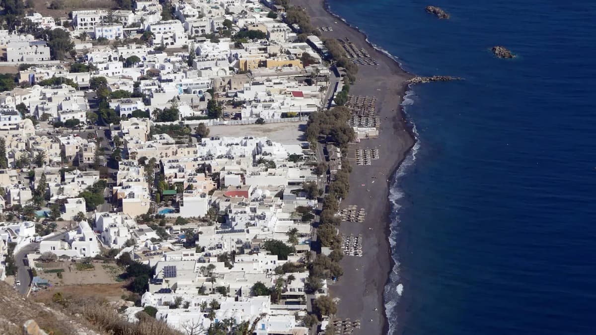 Aerial view of Kamari black sand beach in Santorini with azure waters and white buildings along the coastline