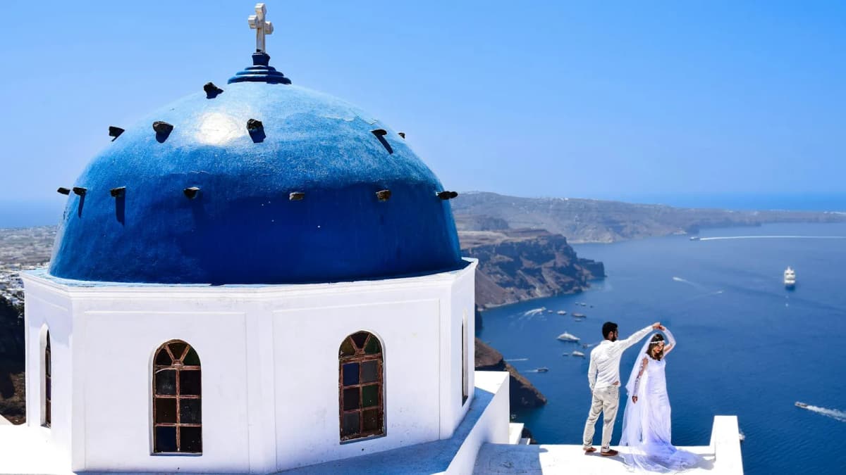 Wedding couple dancing beside a blue dome church overlooking the Santorini caldera and Aegean Sea