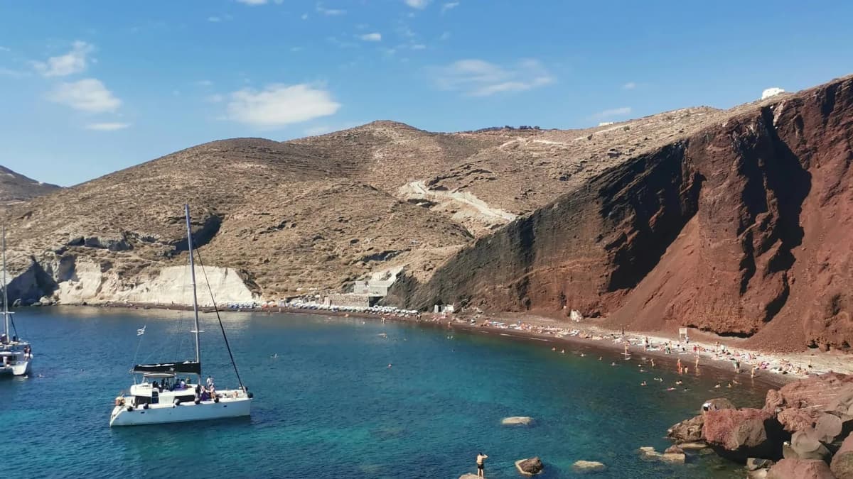 Crystal clear waters and red volcanic cliffs at a Santorini beach with turquoise Aegean Sea