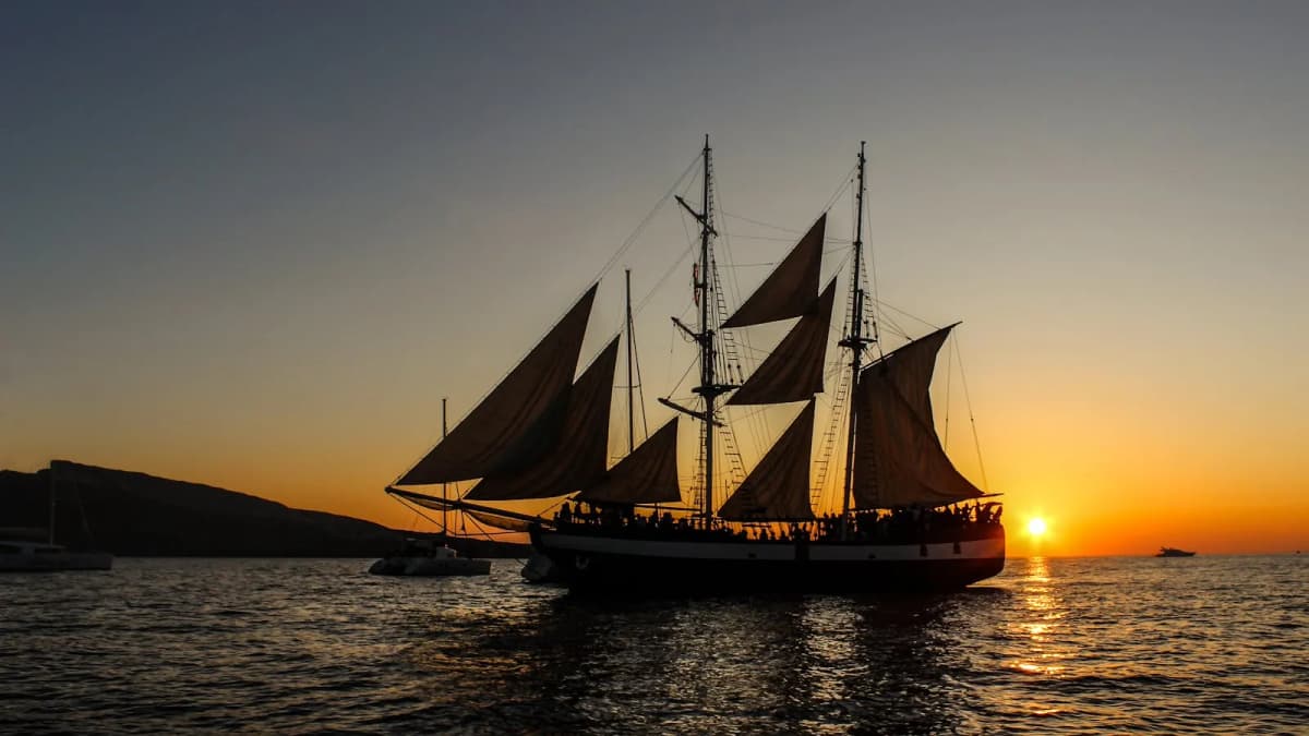 Catamaran sailing past Santorini cliffs during a golden sunset cruise on the Aegean Sea