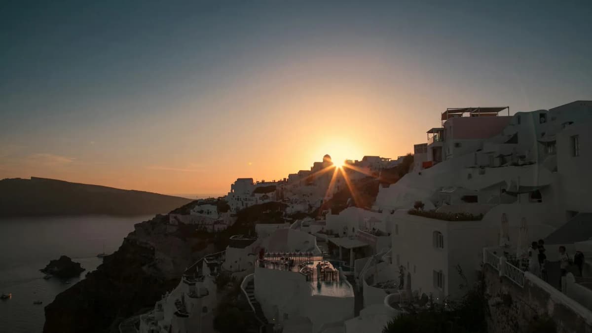 Sun setting over Santorini caldera with whitewashed buildings, capturing the golden hour glow