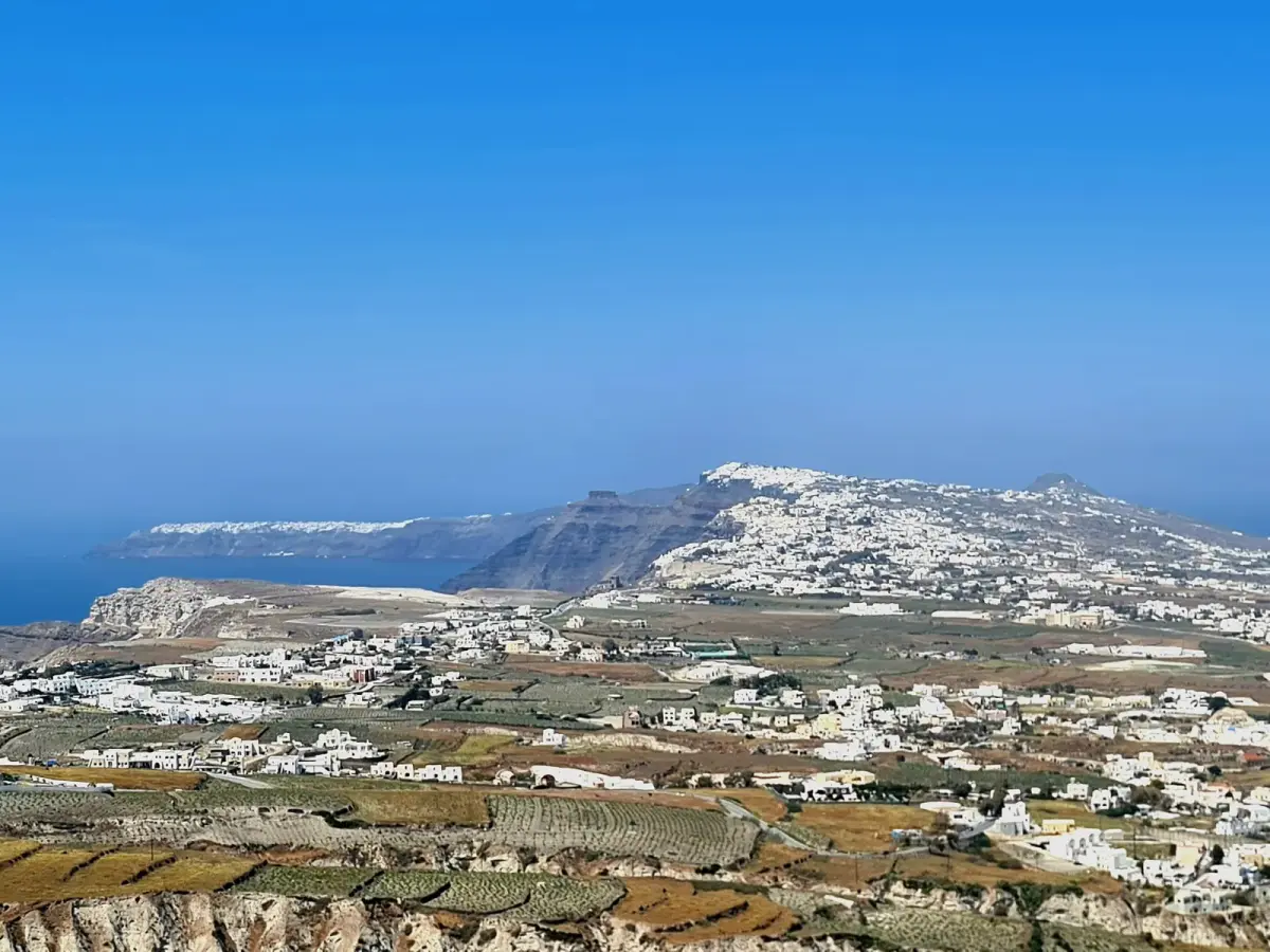 Vineyards and villages on the plain below Pyrgos, with Fira and Oia along the caldera ridge