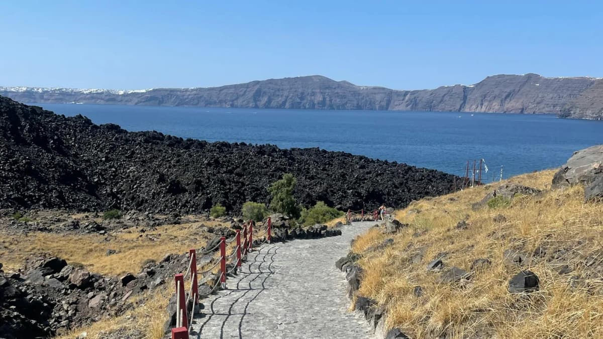 Volcanic hiking trail on Nea Kameni island with Santorini caldera cliffs in the background