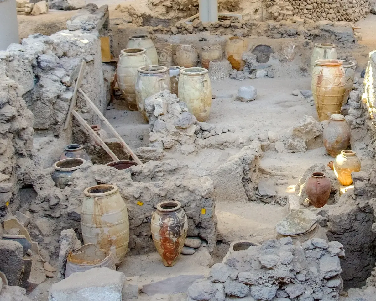 Large clay storage jars still standing among the excavated walls at Akrotiri