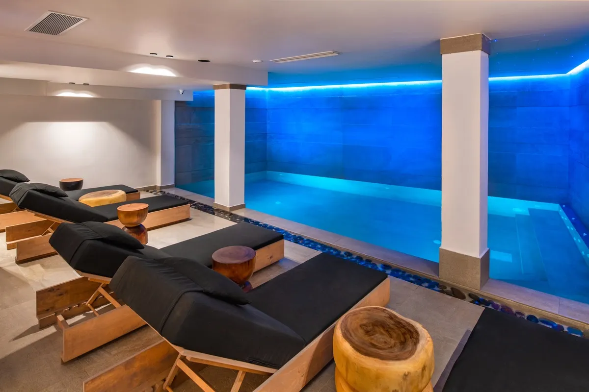 Uma Ray Suites indoor heated pool with blue ambient lighting and lounge chairs