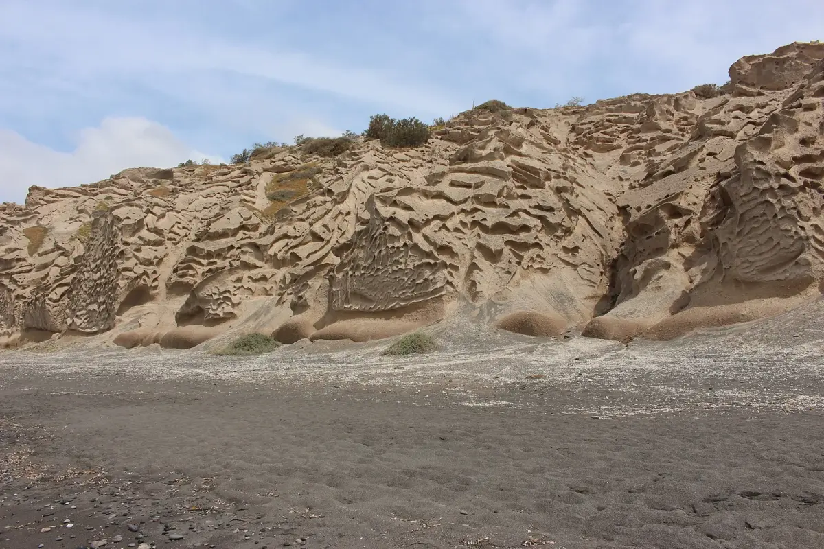 Wind-carved pumice cliffs above the dark sand at Vlychada