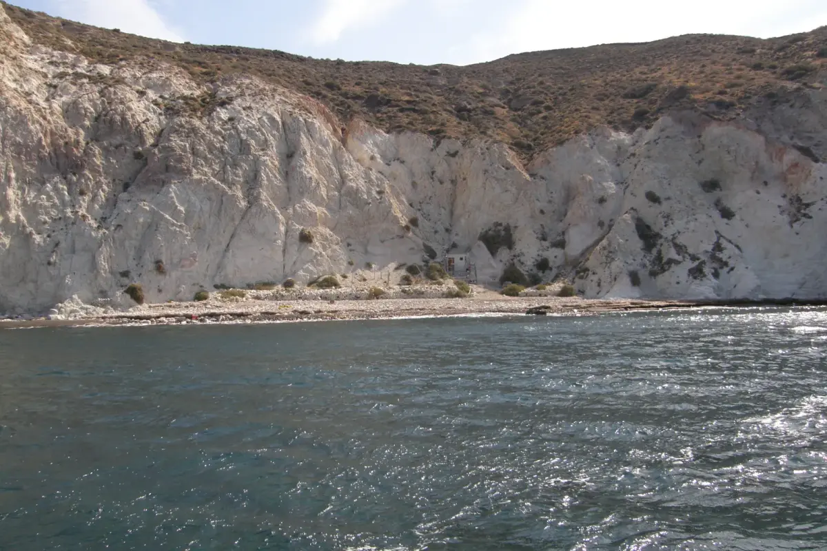 White Beach (Aspri Paralia) in Santorini seen from the sea, tall white cliffs above a narrow pebble beach