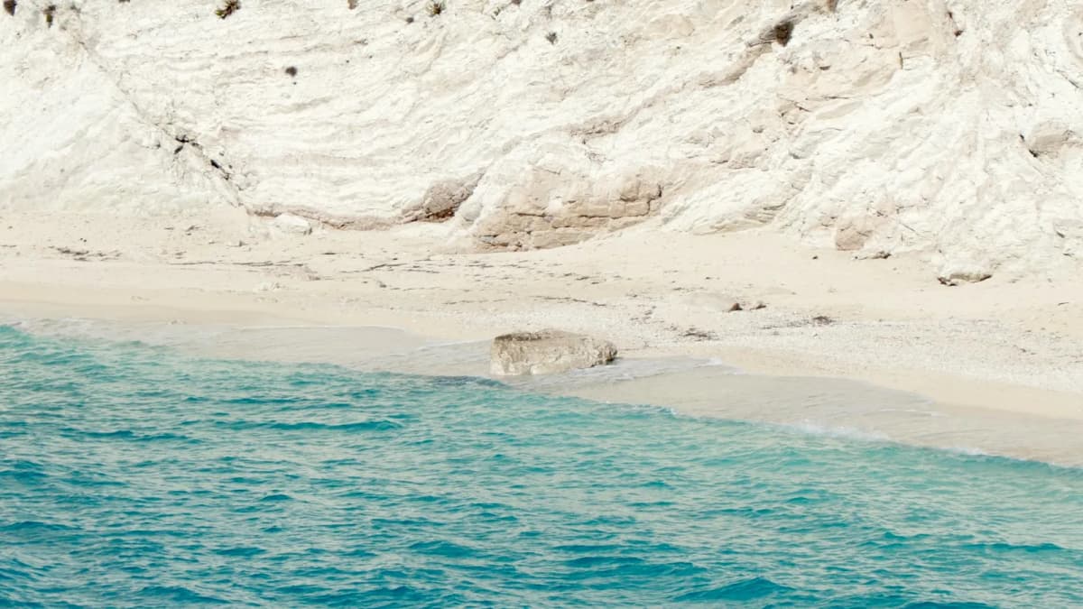 White volcanic cliffs towering over turquoise water at White Beach Santorini