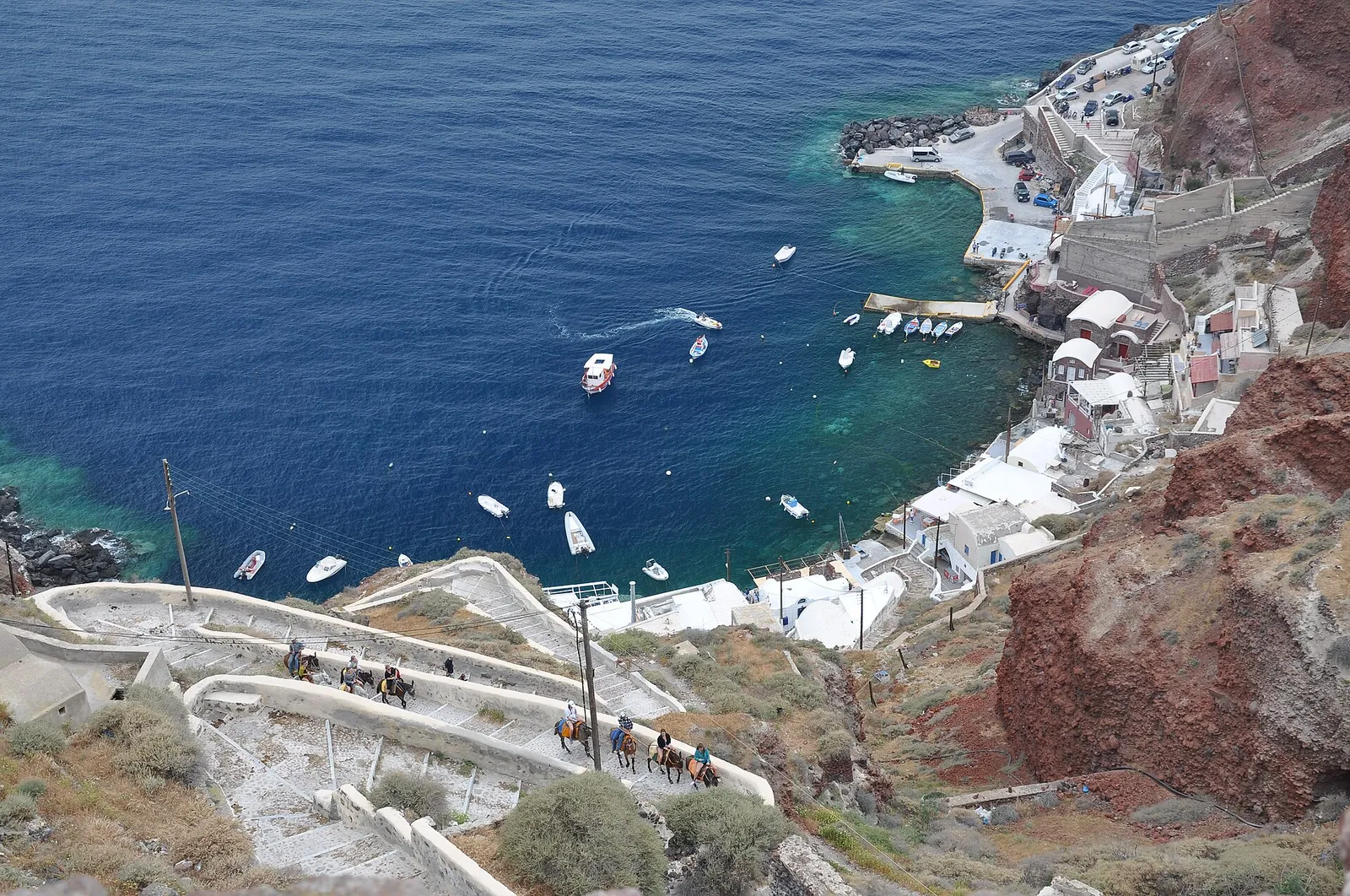 Ammoudi Bay from above, the stepped path zigzagging down the red cliff to the harbour