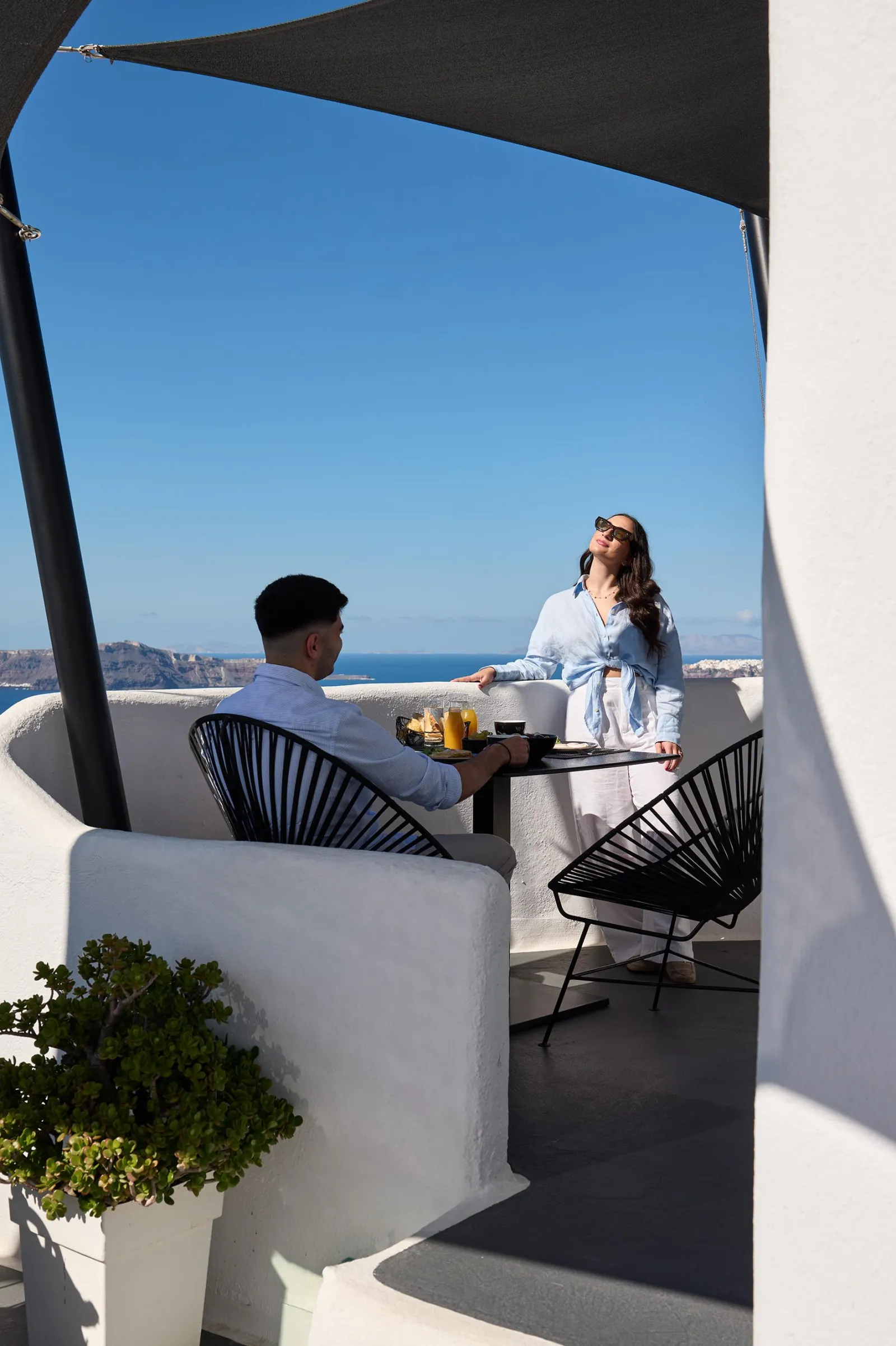A couple on a shaded terrace at Aroma Suites in Fira, the caldera behind them