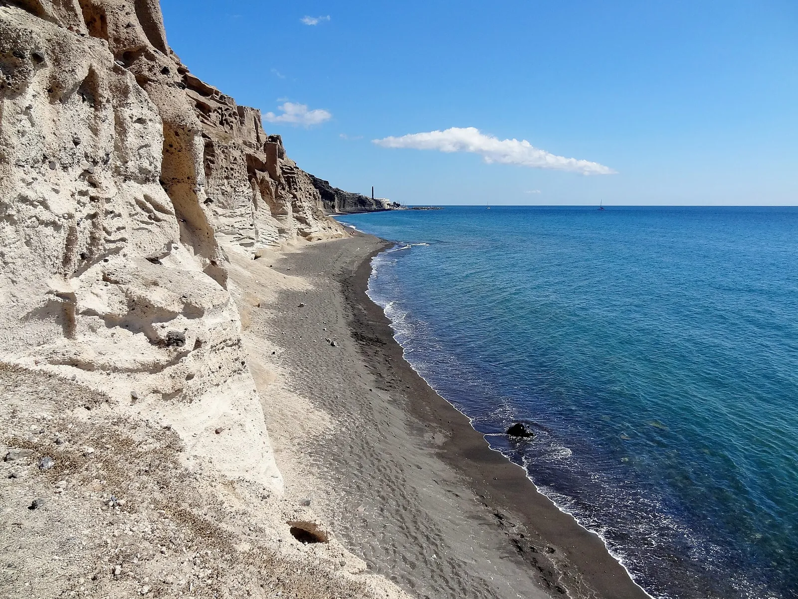 Narrow dark beach under pale pumice cliffs on the south coast near Vlychada