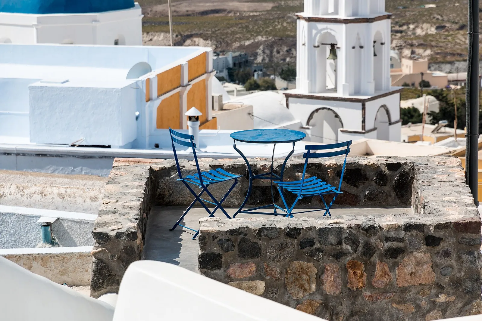 Blue table and two chairs on a stone terrace in Pyrgos, a white bell tower behind