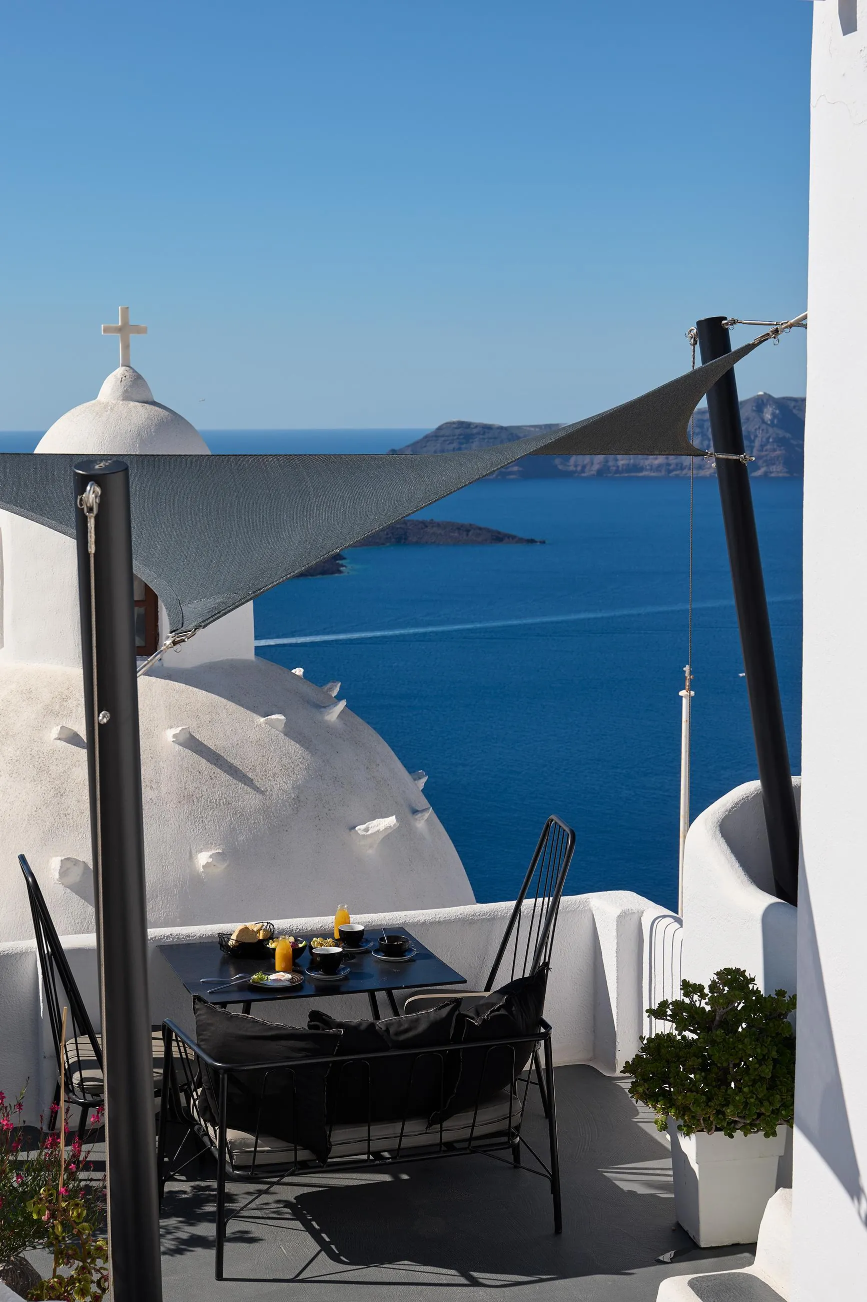 Breakfast table on a terrace next to a white church dome, facing the caldera in Fira