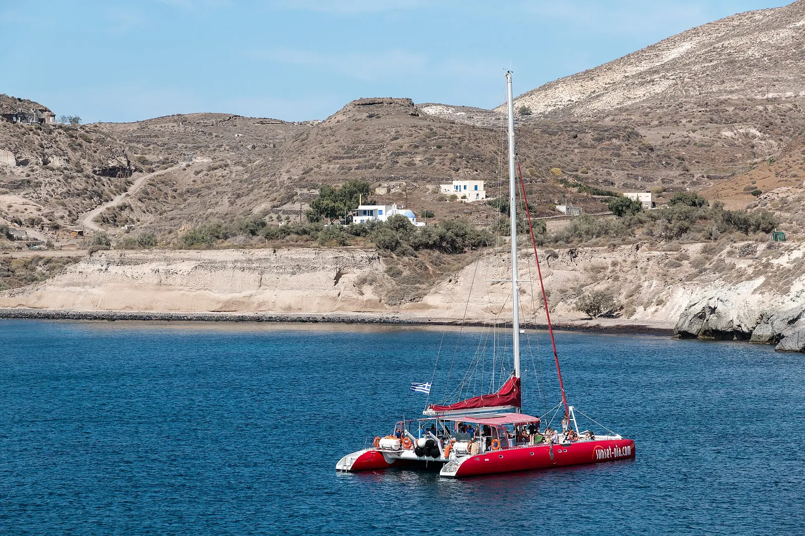 Red catamaran at anchor in a bay near Akrotiri, Santorini, people on deck