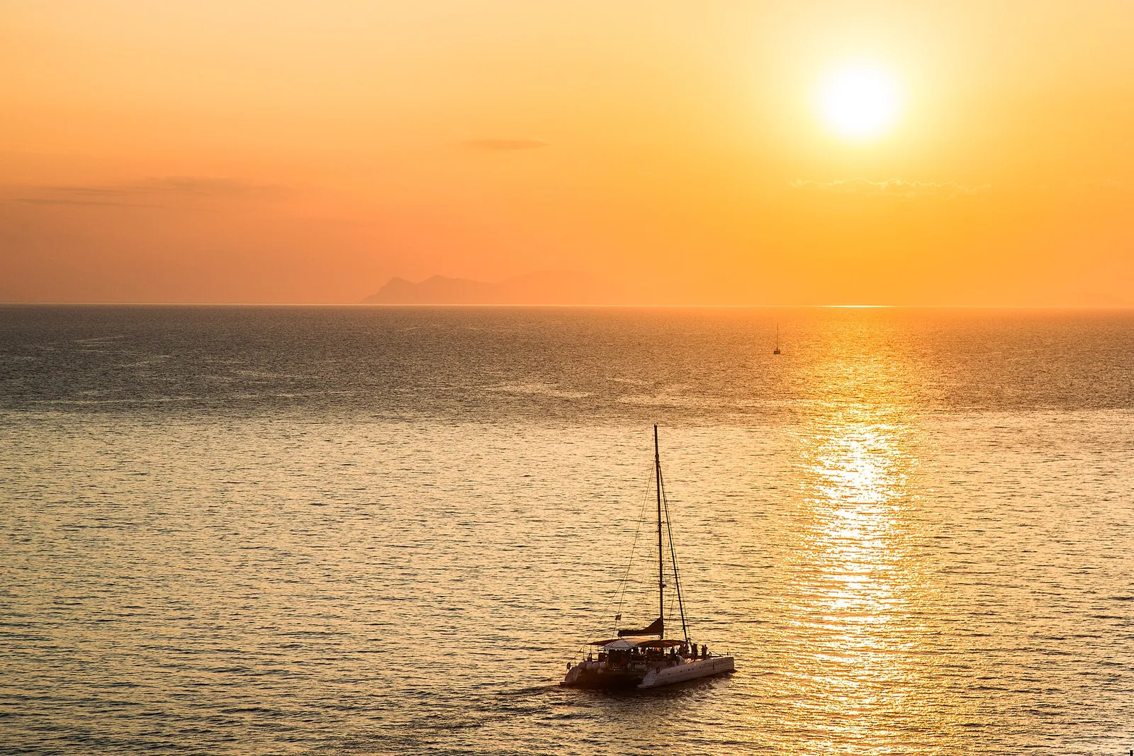 Catamaran sailing towards the low sun on a gold sea off Santorini