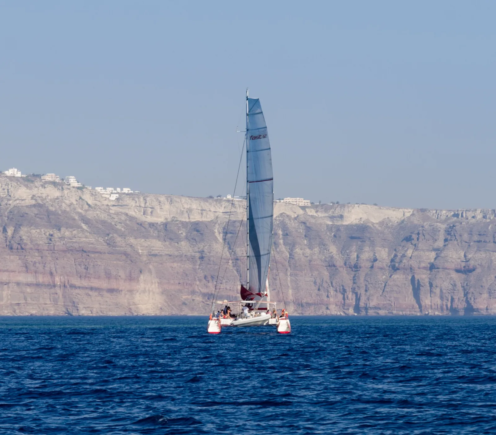 A catamaran under sail in the caldera near Palea Kameni, the Santorini cliffs behind