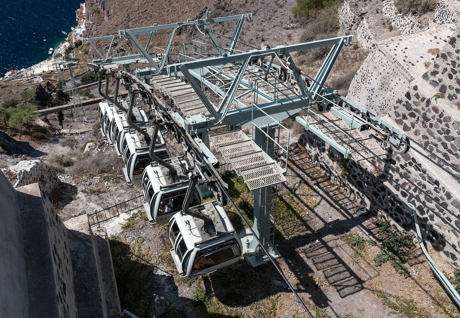 Cable car cabins hanging below the upper station in Fira, the zigzag steps on the cliff beside them