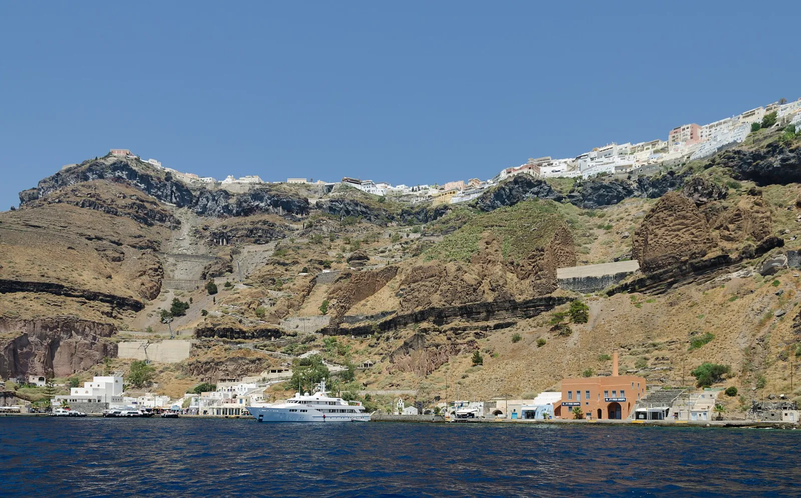Fira's Old Port at the foot of the caldera cliffs, with the cable car line and the zigzag steps climbing up to the town