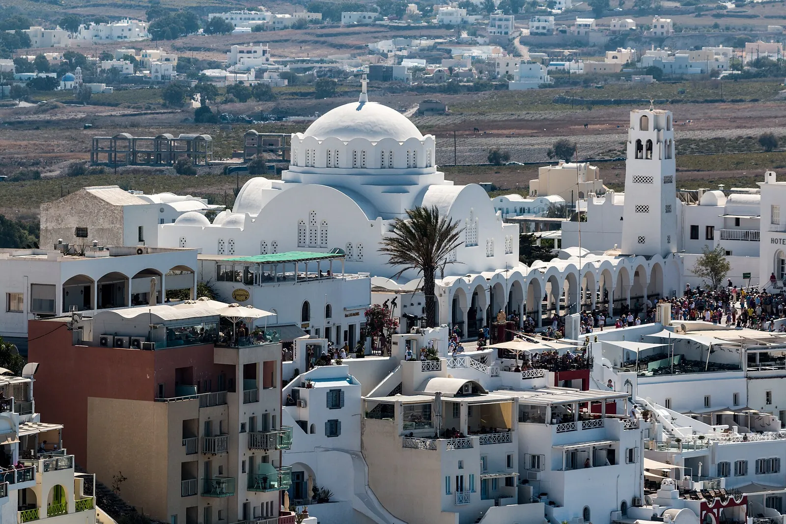 Fira's rooftops around the white Orthodox cathedral and its bell tower, with the inland plain beyond
