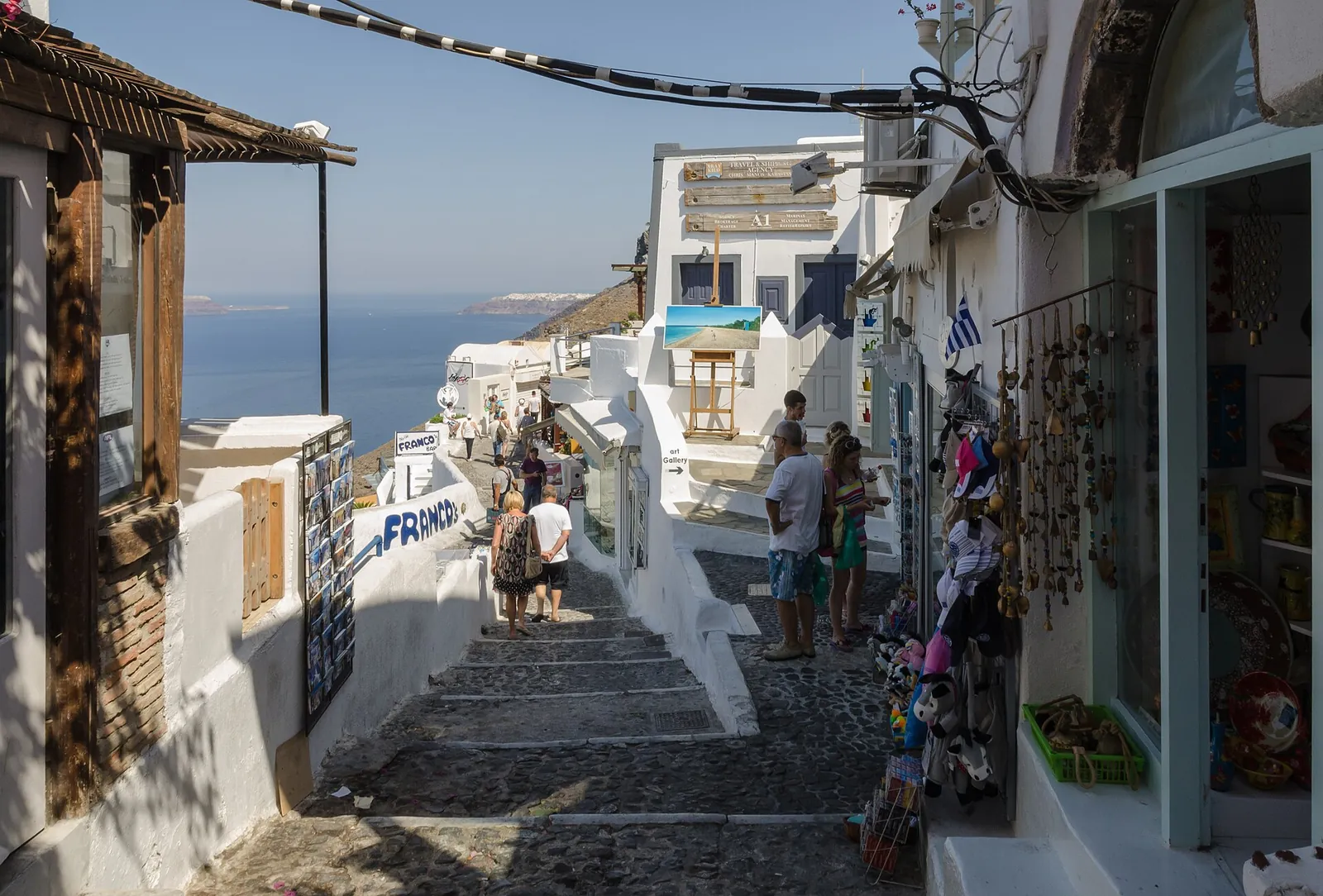 Stepped lane of shops and cafes along the caldera rim in Fira, the sea at the end