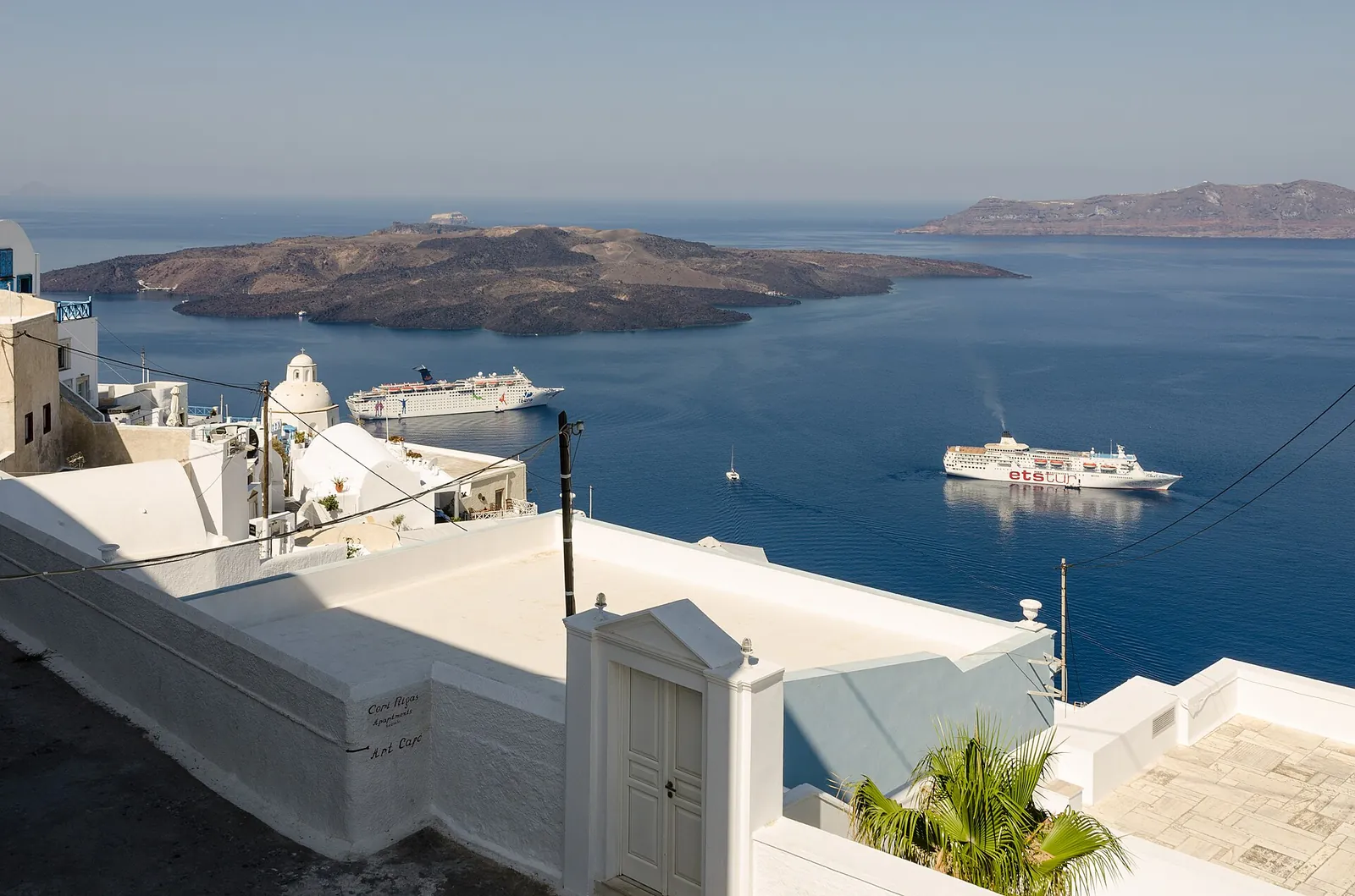 View from a whitewashed lane in Fira over the caldera to Nea Kameni, a cruise ship below