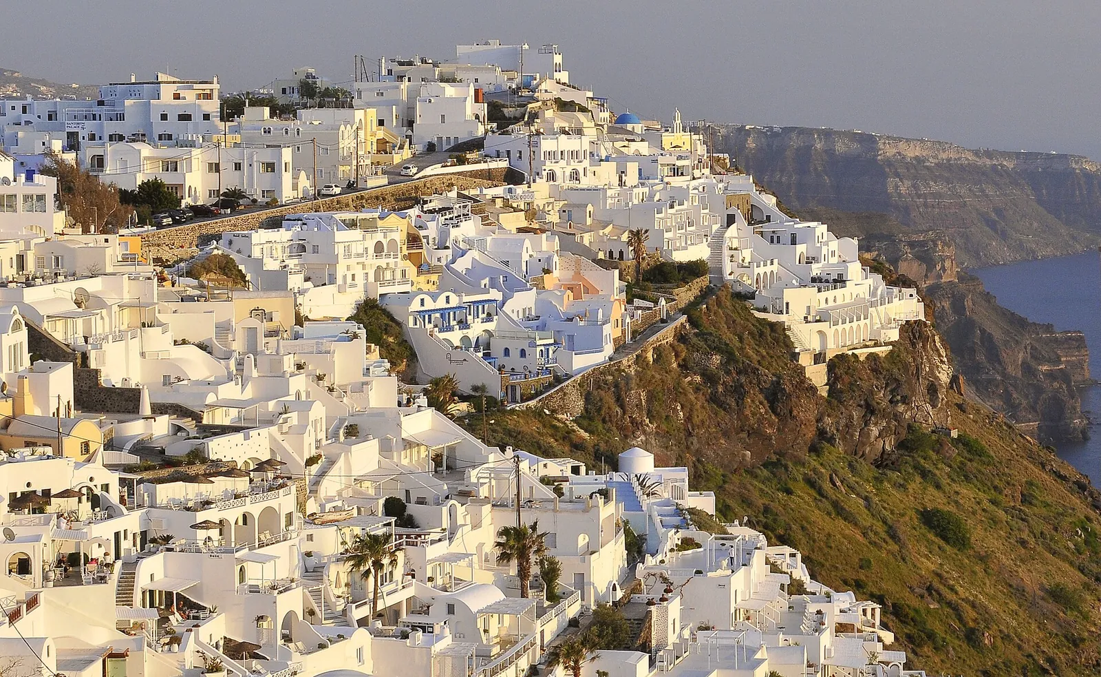Whitewashed houses stepping down the caldera cliff north of Fira in warm evening light