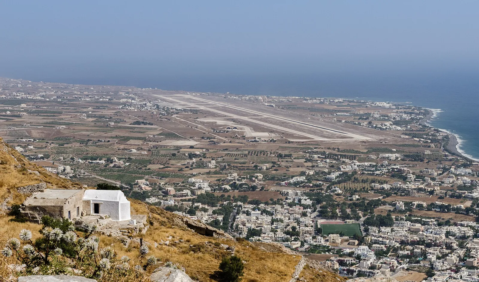White chapel on the slope above Kamari, with the airport runway and the east coast below