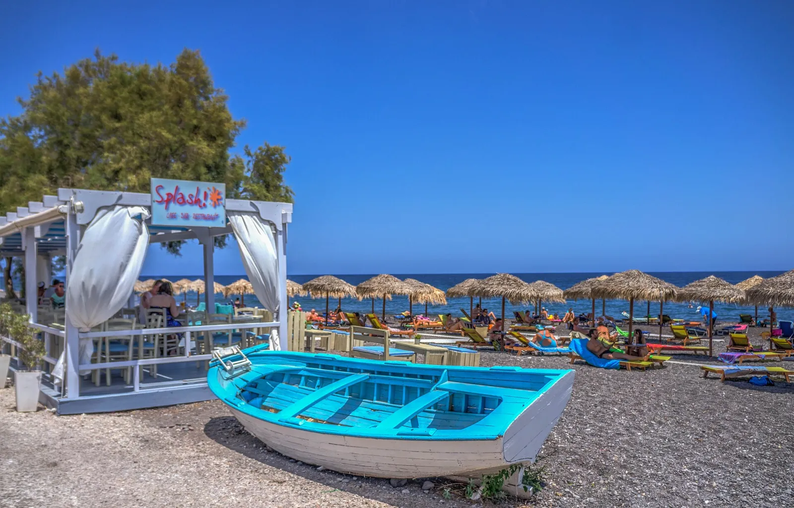 Black sand beach at Kamari in Santorini, with a wooden boat on the shore and umbrellas along the sea
