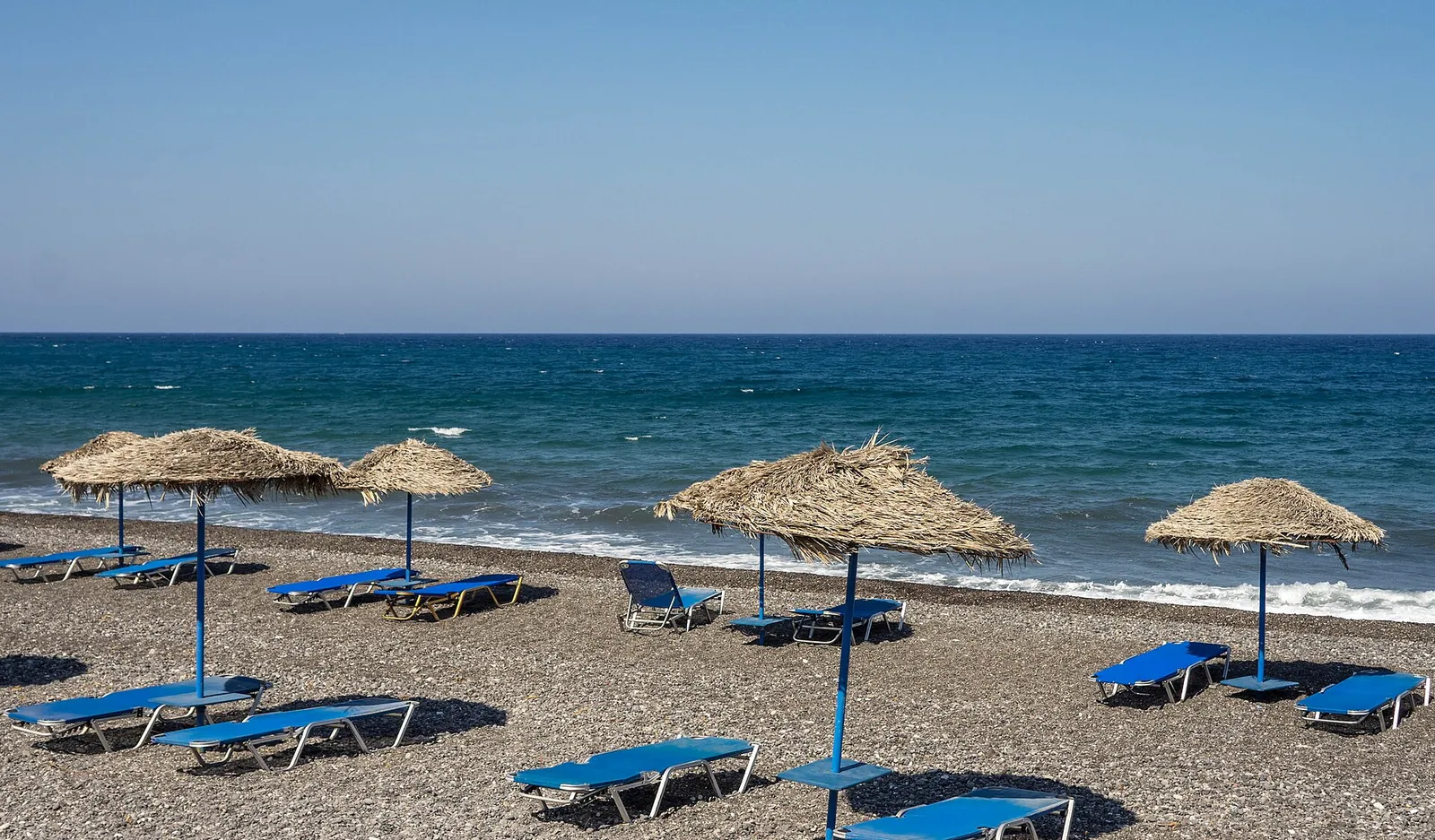 Straw umbrellas and blue sunbeds on Kamari's dark beach by the sea