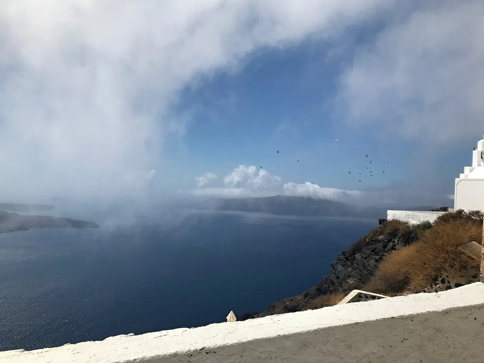 Low cloud spilling over the caldera, seen from the path at Imerovigli beside a white chapel