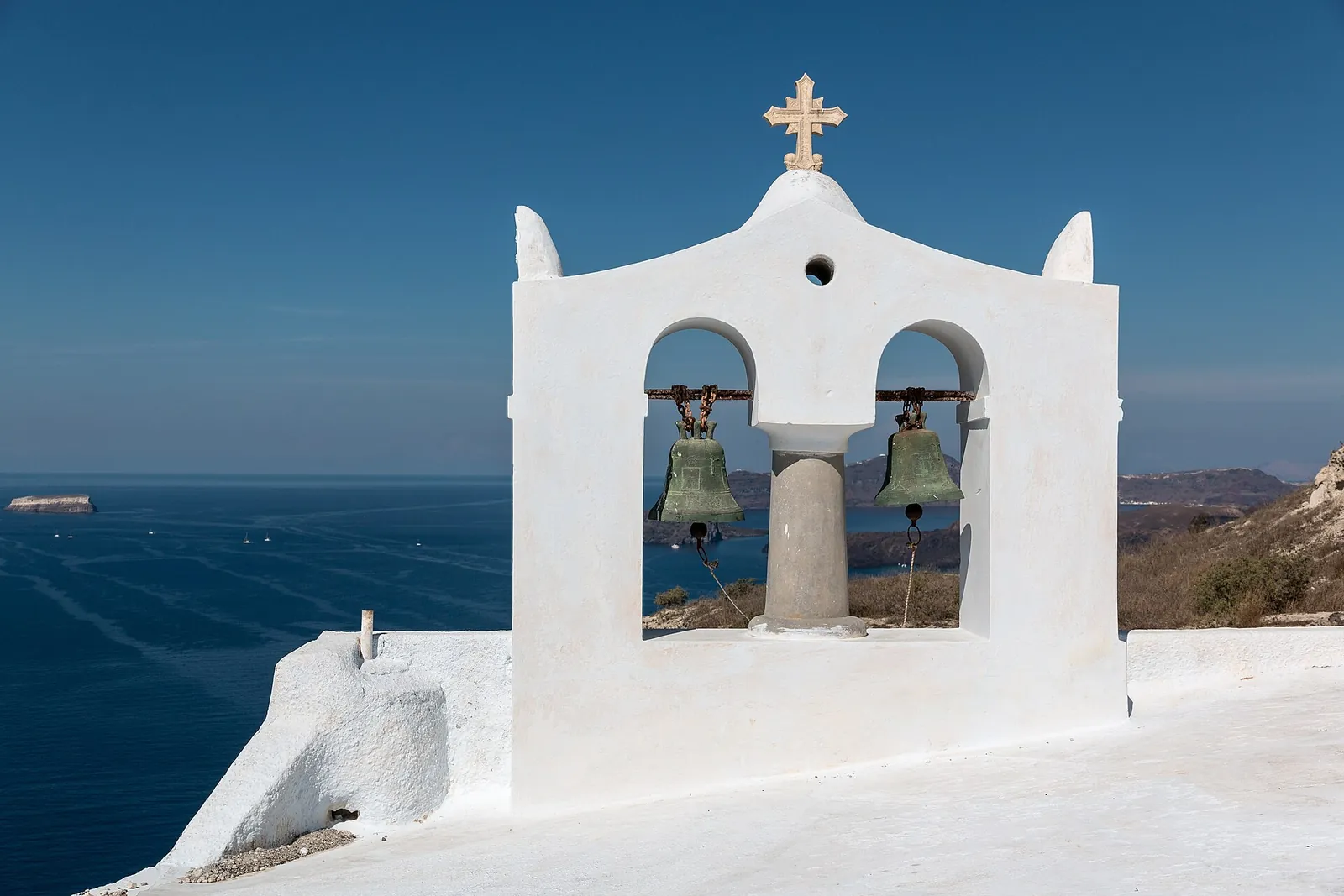 White bell arch of a chapel in Megalochori, the caldera sea behind