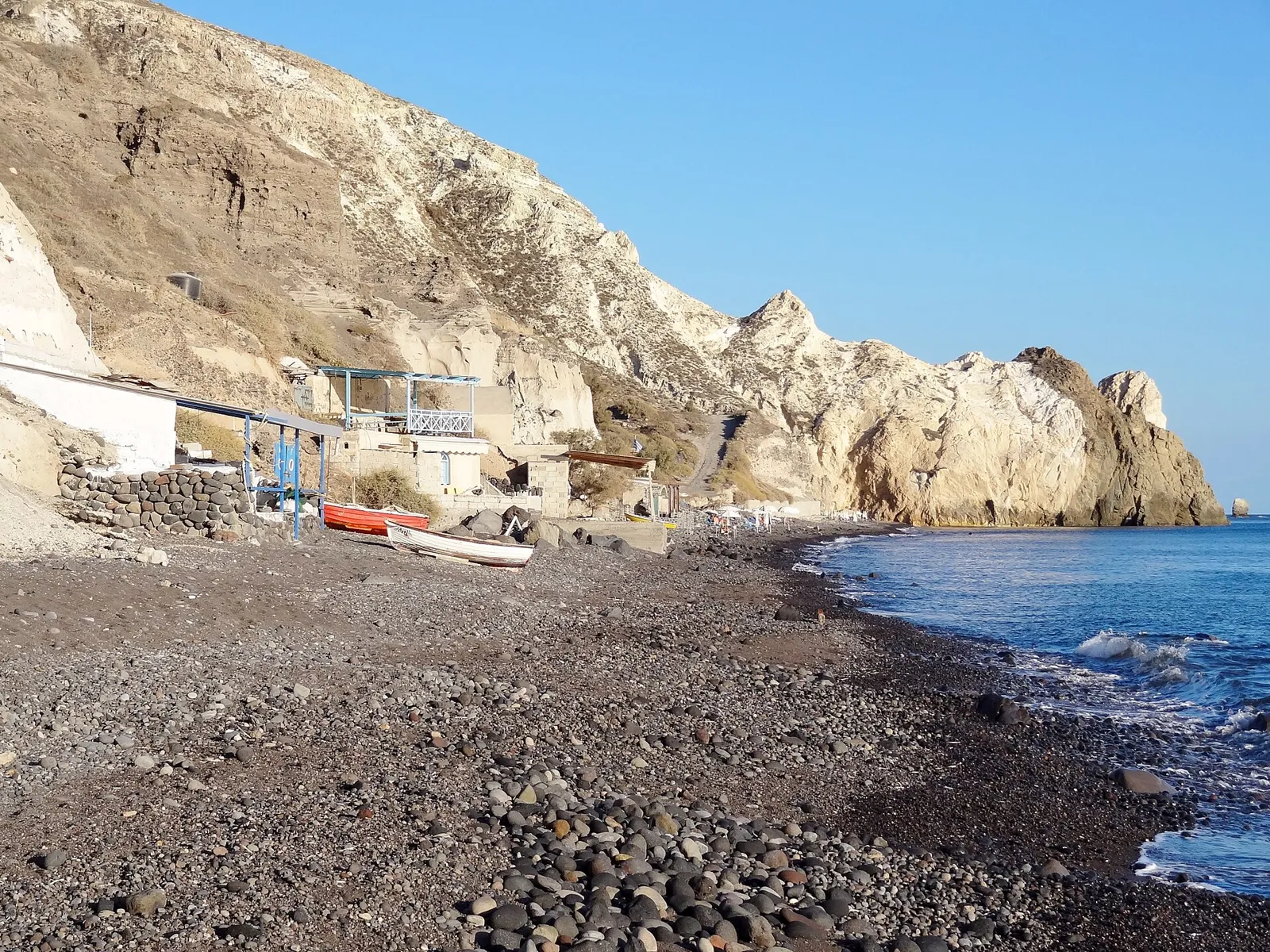 Empty pebble beach at Mesa Pigadia with white cliffs, small boathouses and boats on the shore