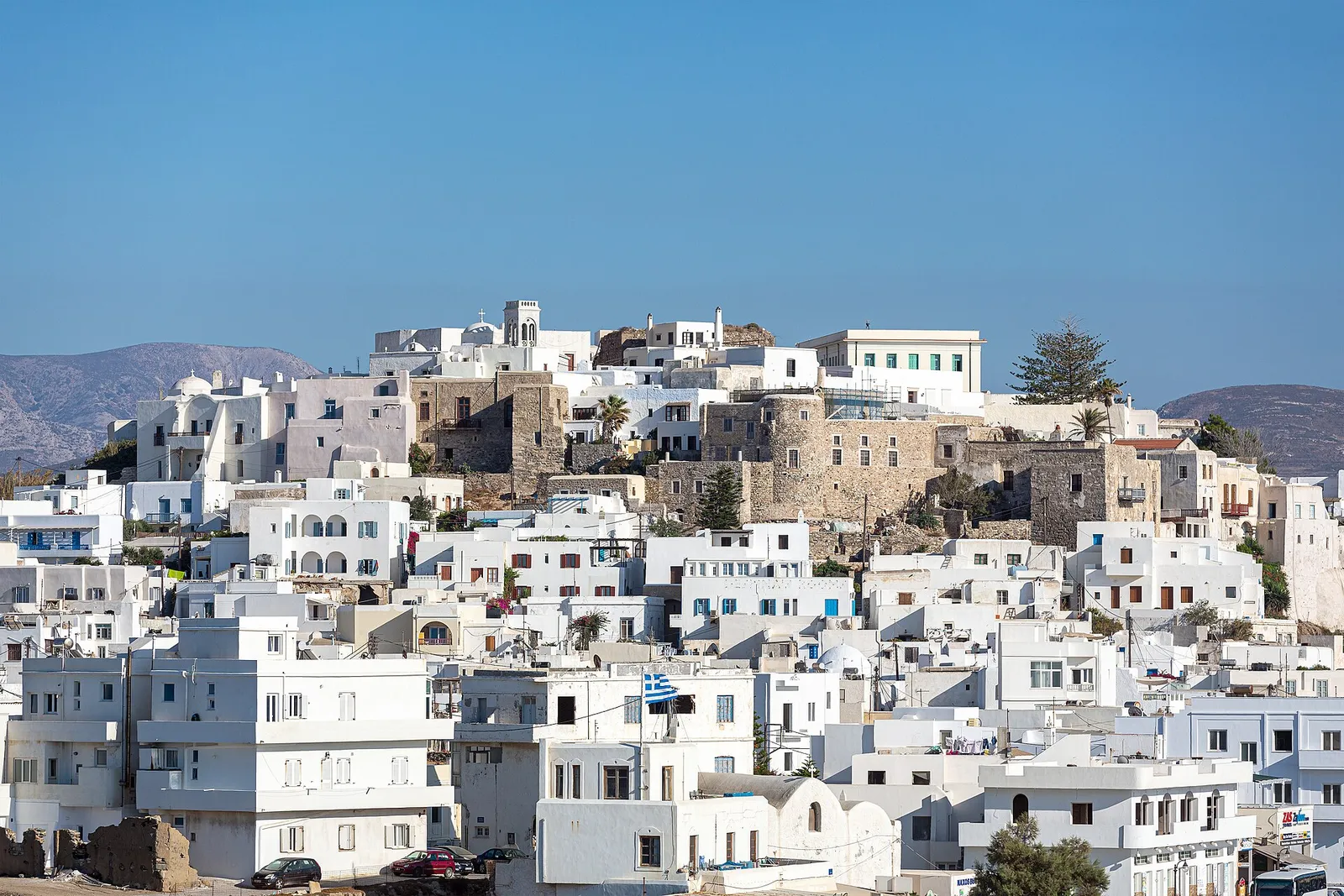 Naxos town seen from the Palatia peninsula: whitewashed houses climbing to the stone Venetian Kastro, with mountains behind