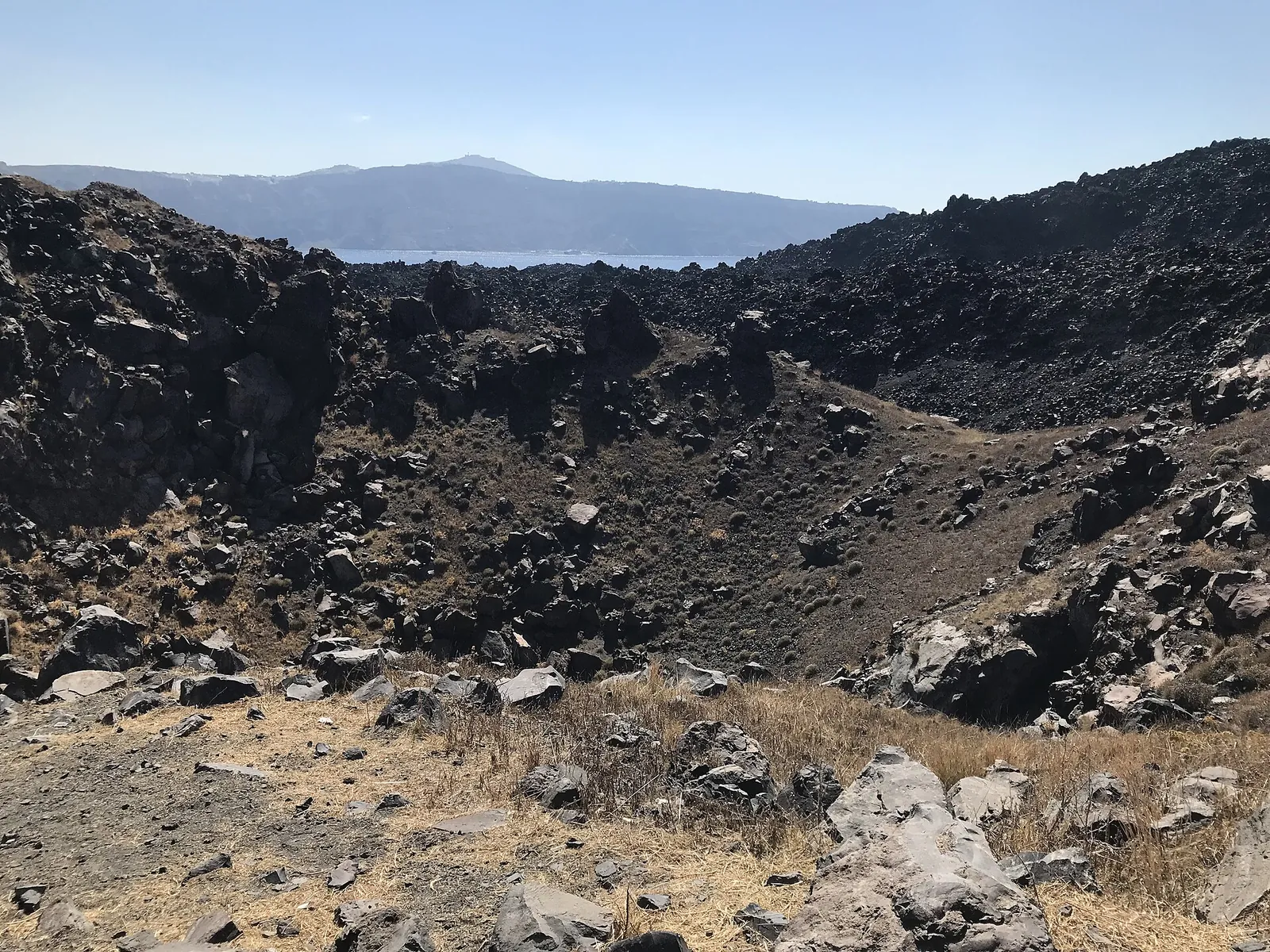 Dark lava rocks around the crater on Nea Kameni, the caldera rim in the distance
