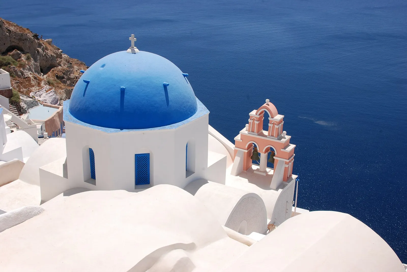 Blue church dome and a pink bell tower in Oia above the deep blue caldera