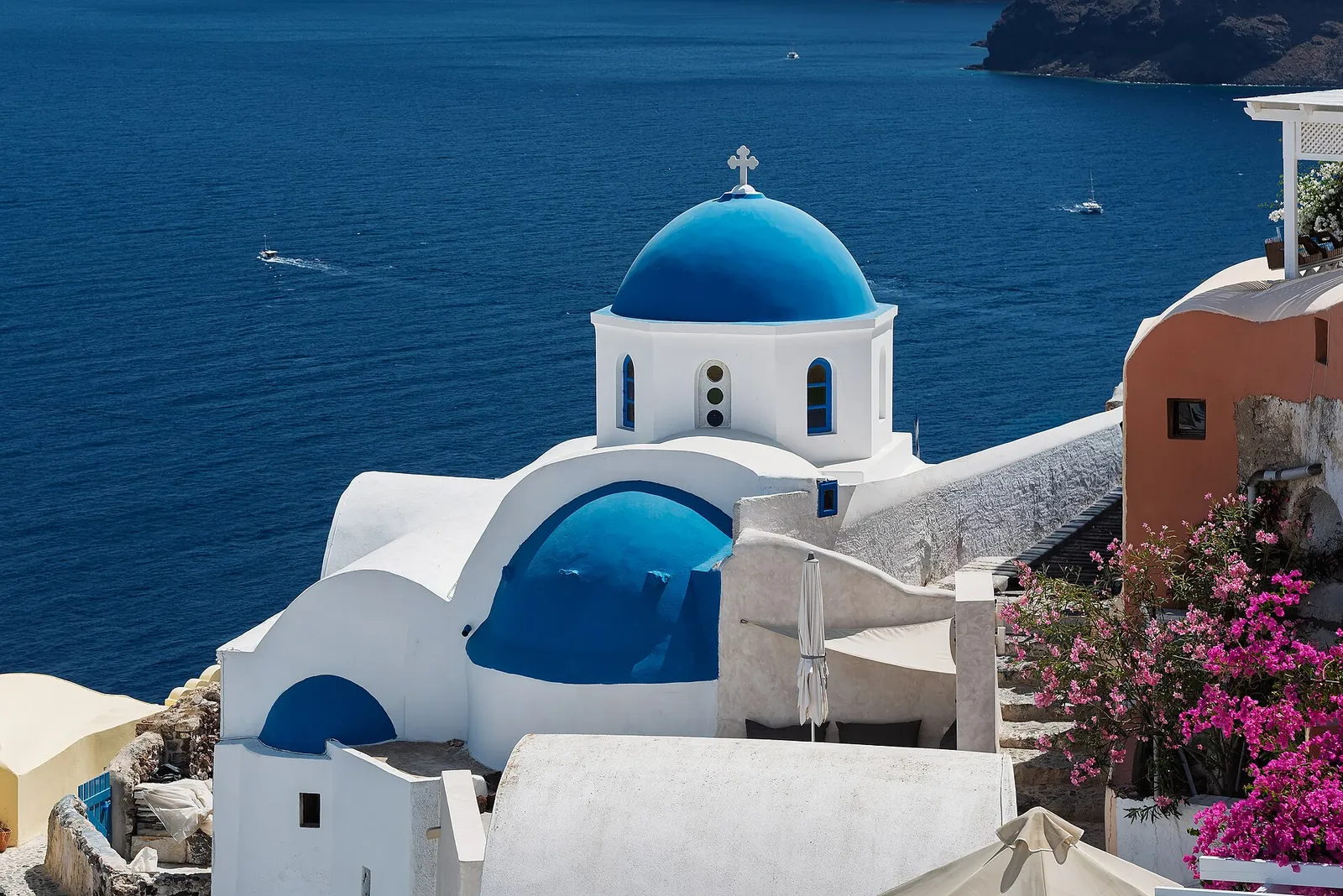 Blue-domed church in Oia with pink bougainvillea, the caldera sea beyond