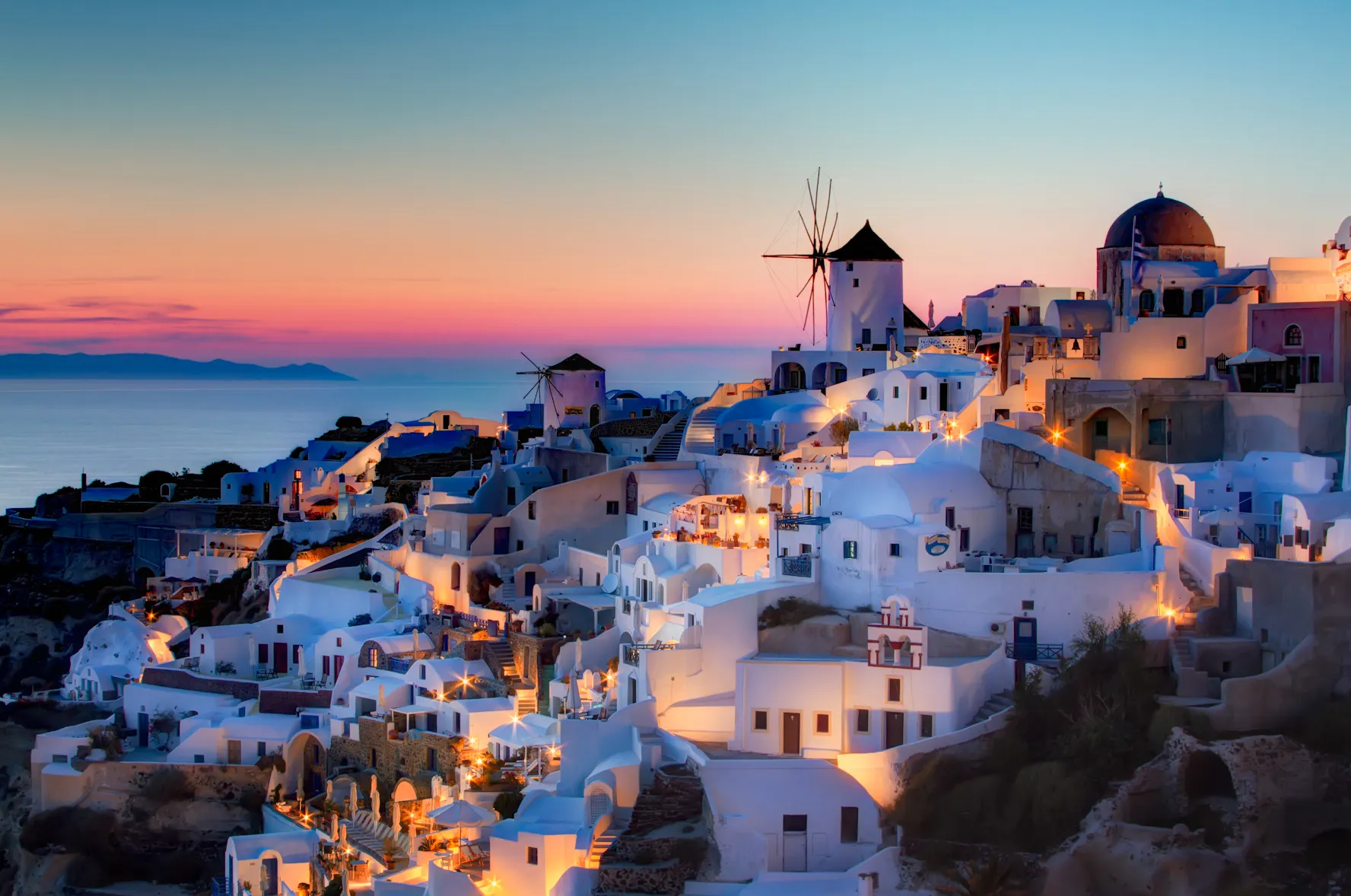 Oia's whitewashed houses and windmills lit up at dusk on the caldera cliff