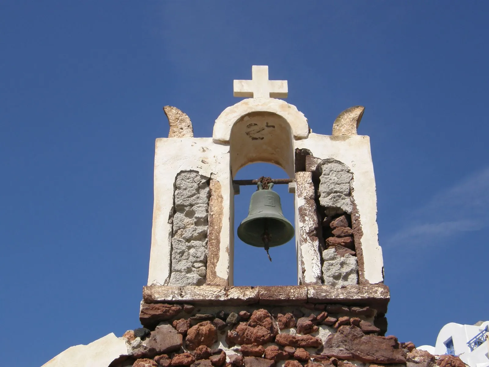 Old stone bell gable with a single bell against a blue sky in Oia