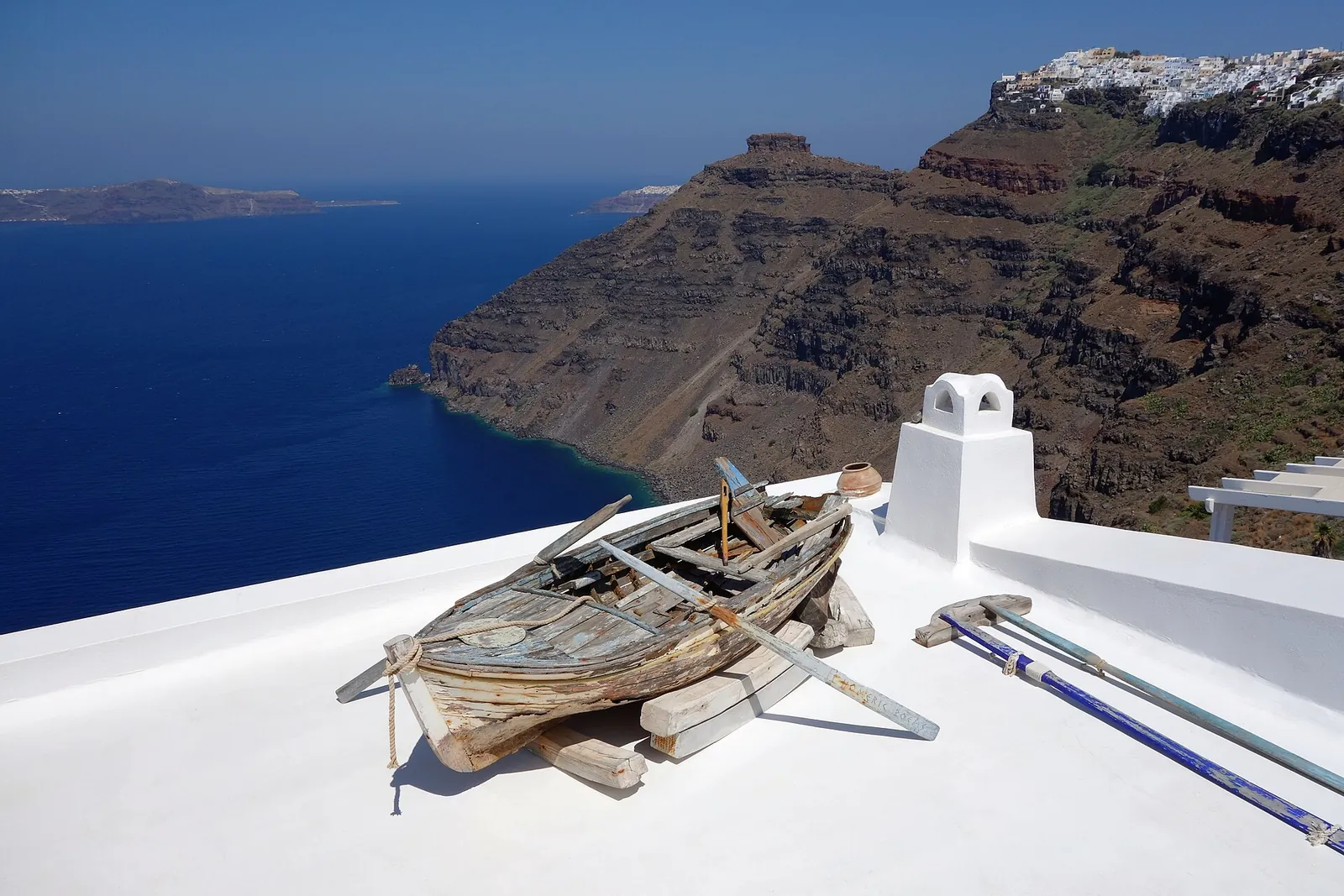 Old wooden rowing boat on a whitewashed rooftop, the caldera cliffs and sea behind