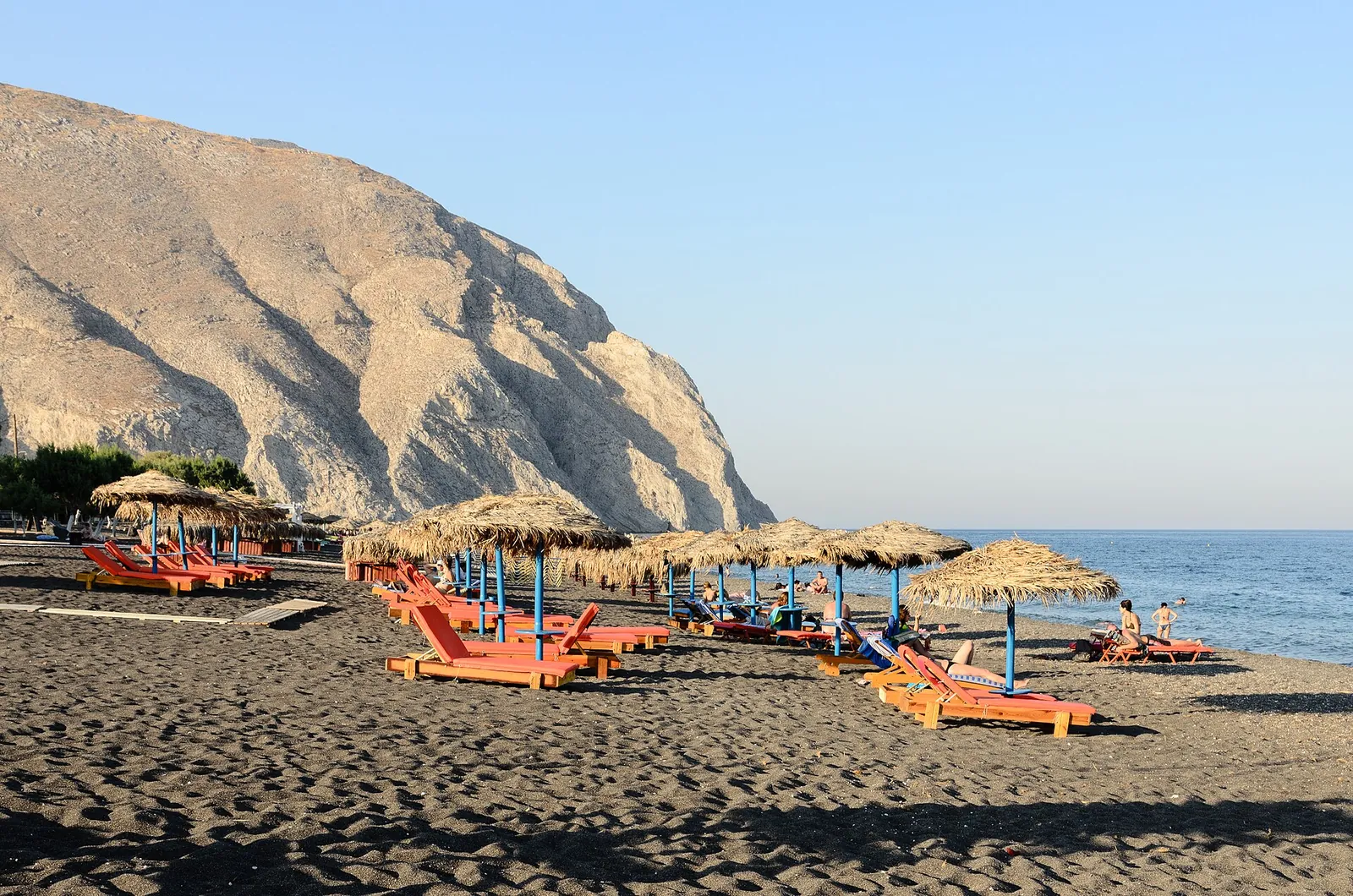 Straw umbrellas and sunbeds on Perissa's black sand below the Mesa Vouno headland