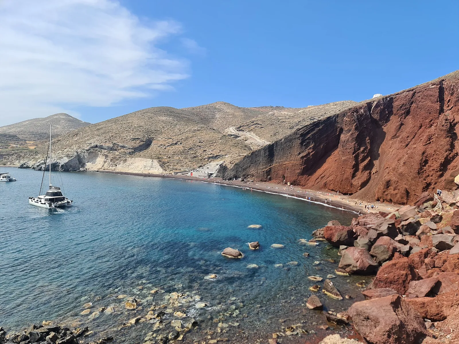 Red Beach's bay under red volcanic cliffs, a catamaran anchored in clear water