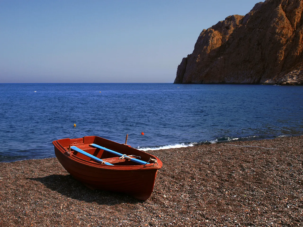 Red rowing boat pulled up on Kamari's dark pebbly sand, the Mesa Vouno cliff behind