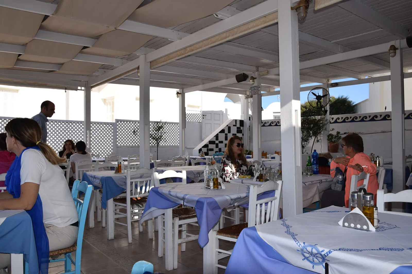 Diners at a covered taverna terrace with blue and white tablecloths in Fira