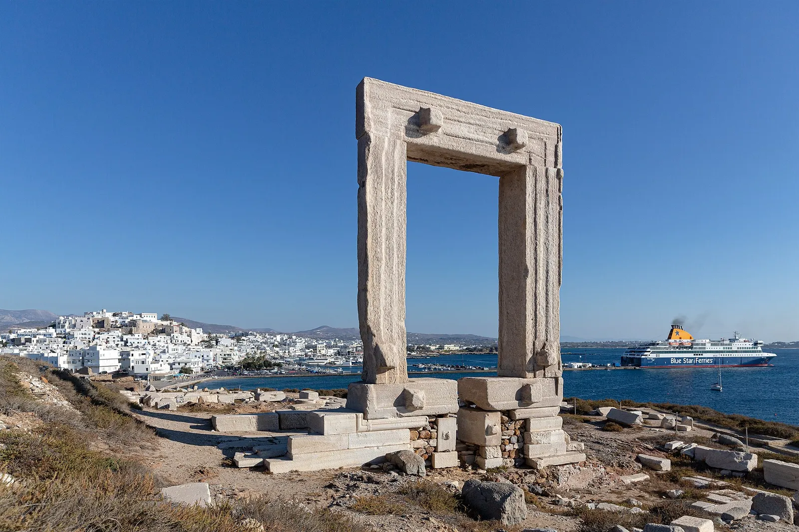 The marble Portara gateway on Naxos, with Naxos town on the left and a Blue Star ferry docked in the harbour on the right